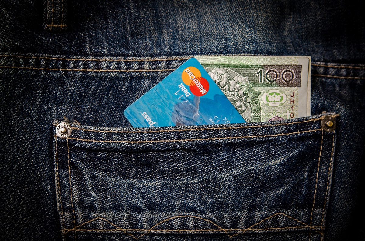 Hands interact with a detailed digital financial dashboard showing budget categories and debt repayment progress, while physical cash and coins are neatly organized on a table beside it, illustrating diligent personal finance management.
