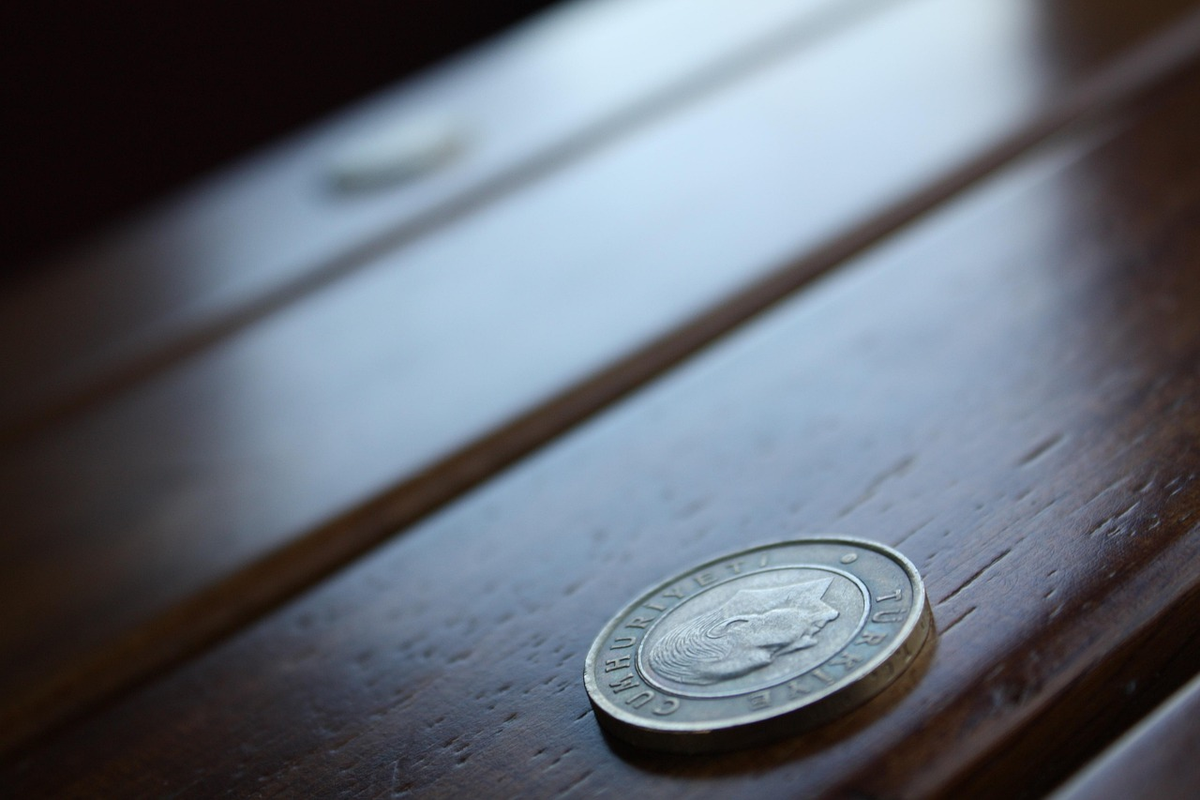A hand thoughtfully distributes diverse financial assets (represented by small, growing plants, miniature buildings, and coins) into separate, secure compartments, while a large, fading banknote in the background visually depicts the impact of inflation and time on unprotected capital.