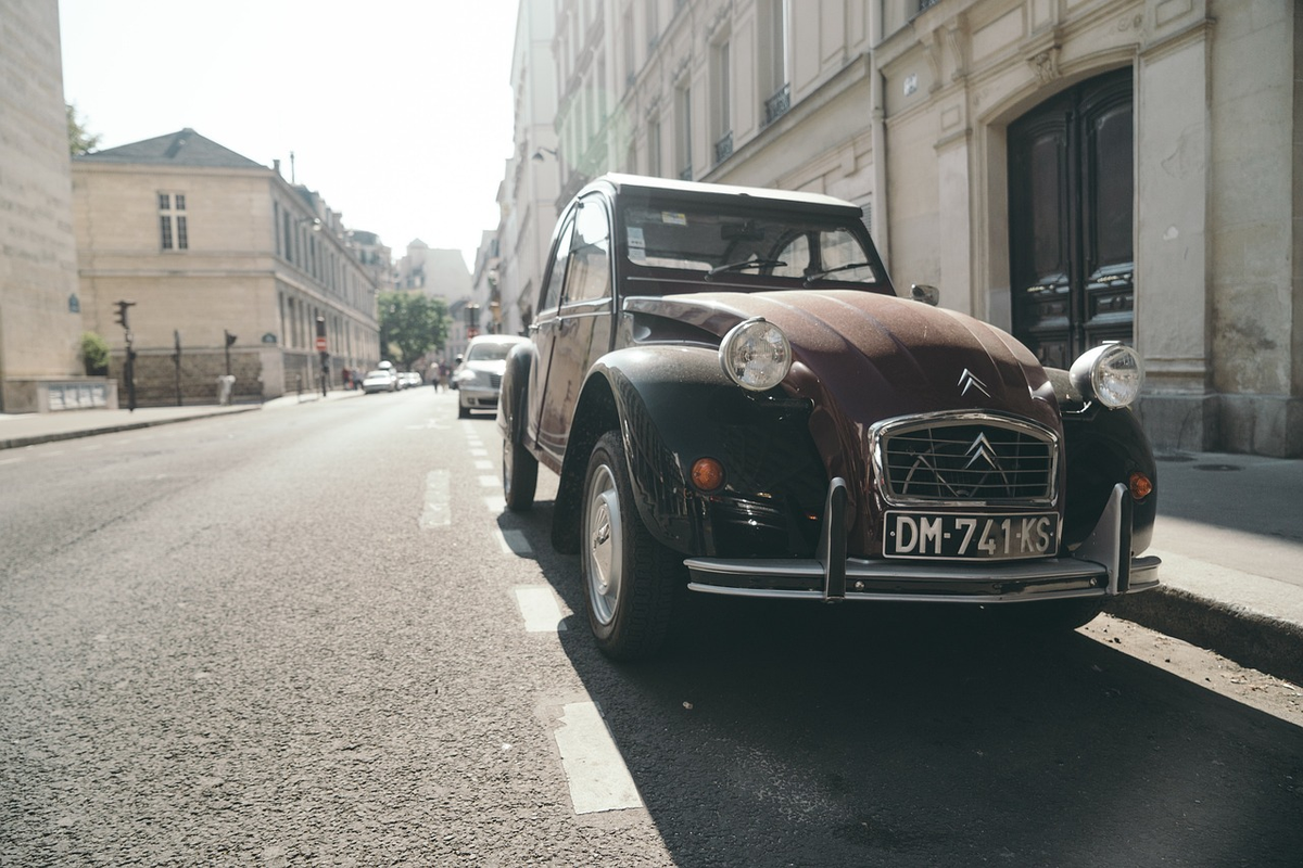 A modern car driving on a road, with a translucent, shimmering financial shield visibly emanating from it, gently encompassing and protecting stylized figures of other people and vehicles, illustrating the concept of third-party liability insurance.